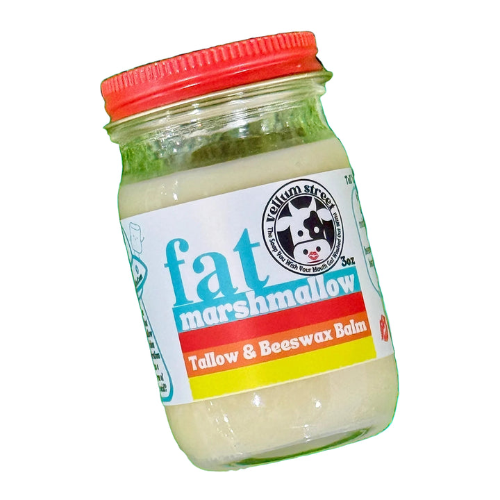 Jar of fat marshmallow balm with a red lid on grass